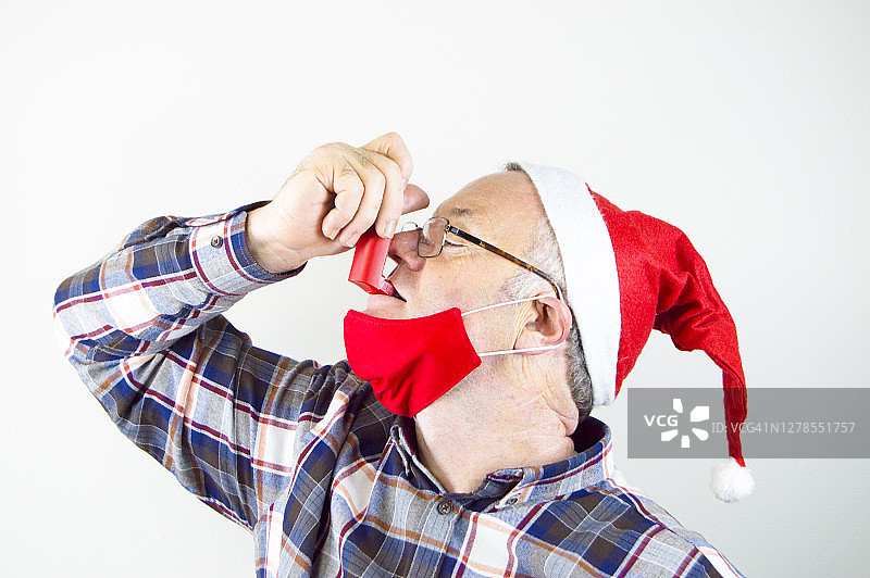 (2019冠状病毒病)戴有红色面罩的圣诞老人帽和使用哮喘吸入器的人图片素材