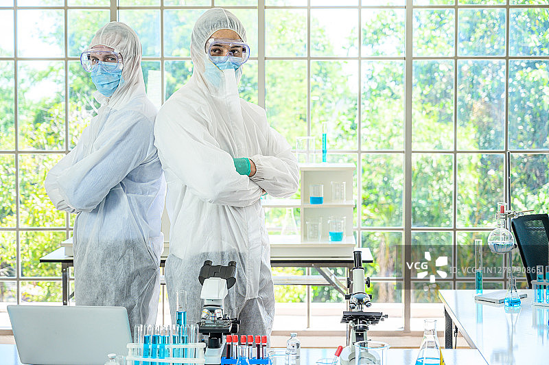 一对男科学家穿着防护服站在
玻璃背景与许多实验室设备在实验室。图片素材
