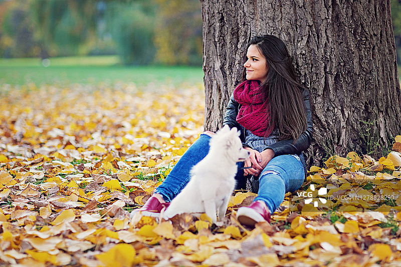 一个年轻的女人和她的狗在秋天的公园里放松图片素材