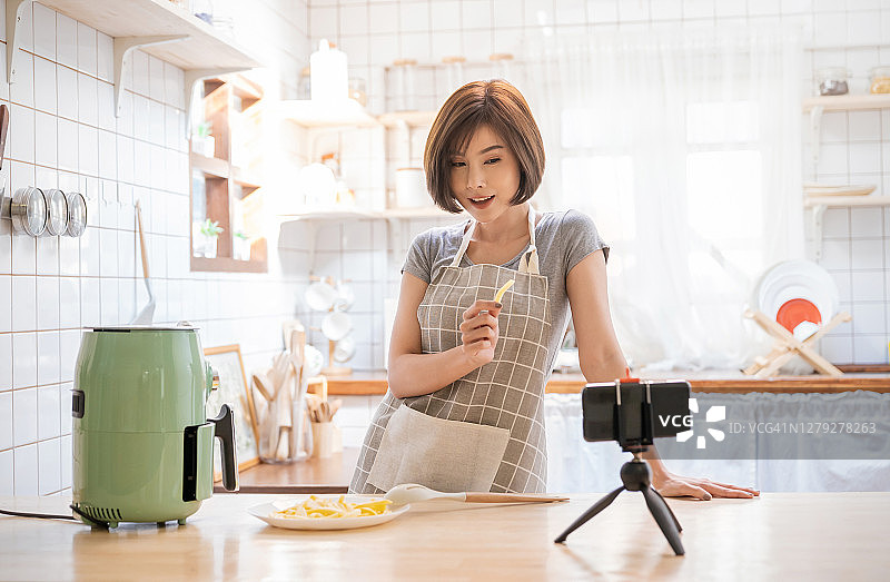 美丽的亚洲女人的肖像评论烹饪土豆食物，用空中飞行智能设备在家里录制直播视频。网红女孩对社交媒体营销、爱好和休闲概念的理解图片素材