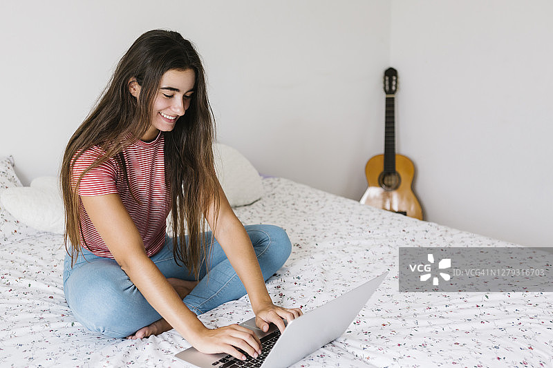 年轻女子坐在卧室里使用笔记本电脑图片素材