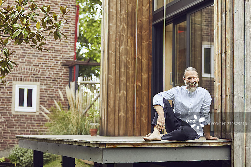 一个快乐的大胡子坐在小房子外面的硬木地板上图片素材
