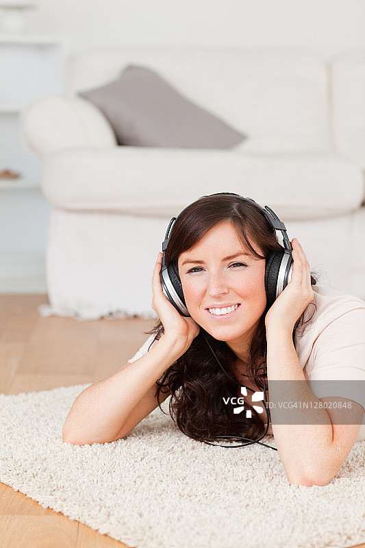 漂亮的黑发女人躺在地毯上戴耳机图片素材