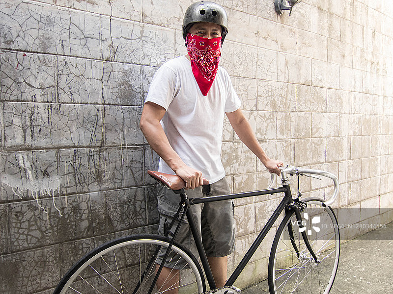 一位年轻的东南亚男子戴着红色头巾，骑着公路自行车外出图片素材