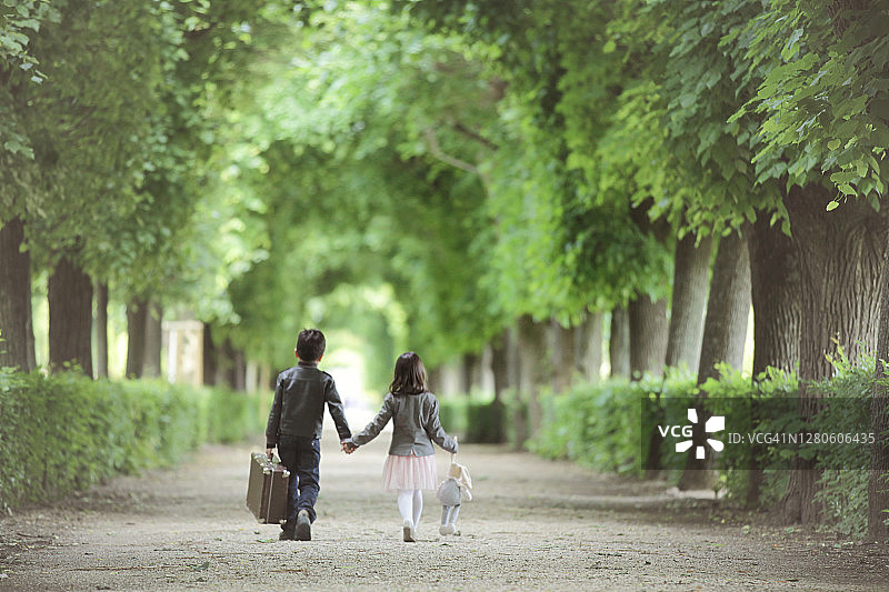 小男孩和小女孩手牵着手，走在美泉宫花园的雕刻花园的后视图。图片素材