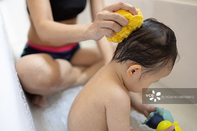 女人在游泳穿给可爱的亚洲婴儿洗头与黄色海绵图片素材