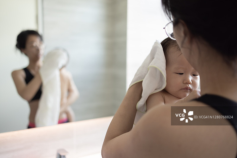 穿着泳装的女士给可爱的亚洲宝宝洗澡后用白色大毛巾擦干她的宝宝图片素材