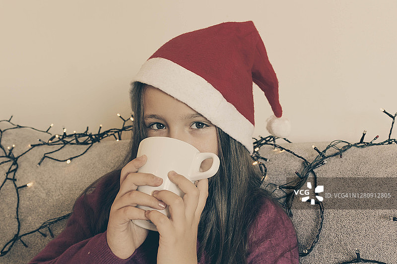 圣诞心情，小女孩戴着圣诞帽喝着热茶或热巧克力图片素材