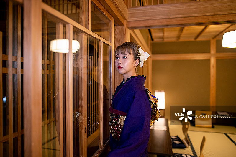 穿着Furisode和服的年轻女子从日式旅馆的榻榻米房间看风景图片素材