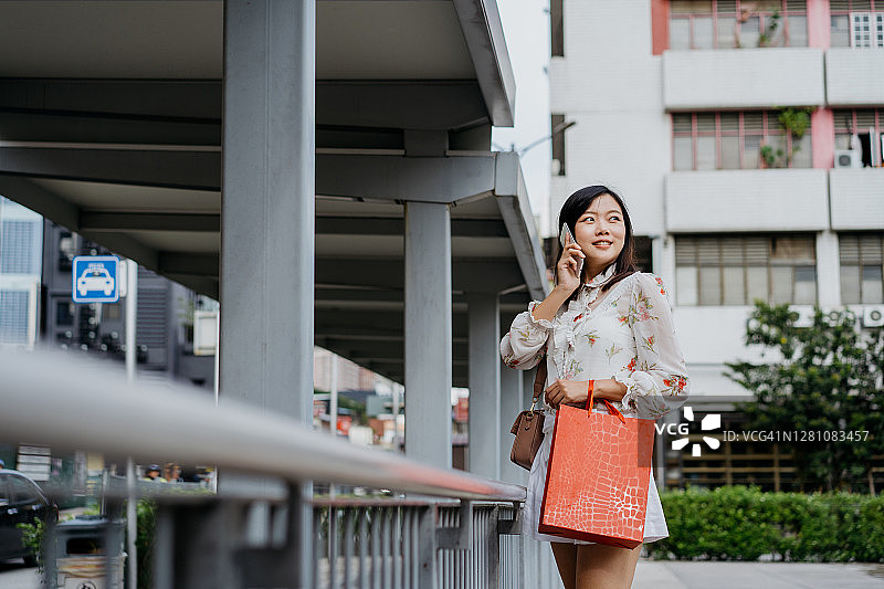 一名拿着购物袋使用智能手机的亚洲华裔女性图片素材