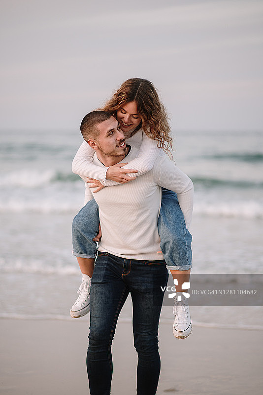 日落时分，一对年轻夫妇在海滩上背着背包散步图片素材