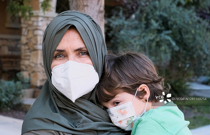 一名成年穆斯林妇女背着儿子回学校，两人都戴着防护口罩图片素材