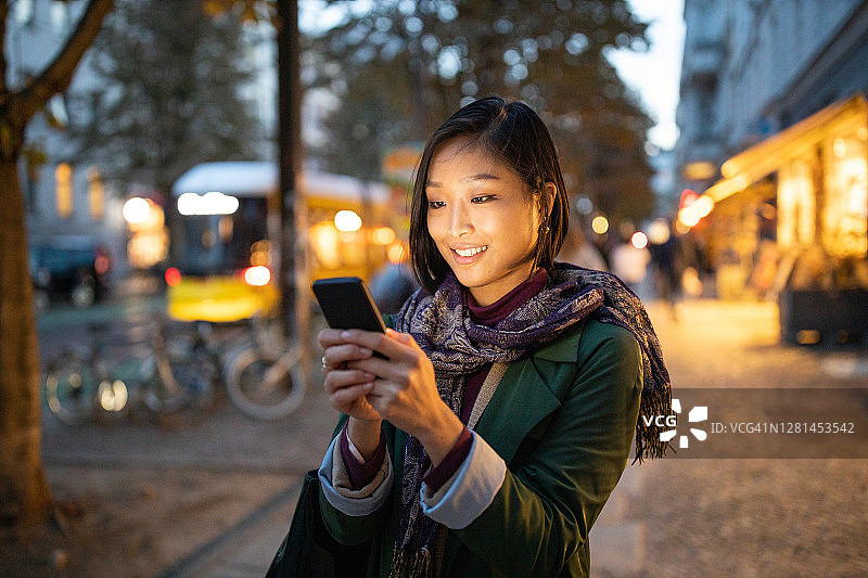 晚上在城市街道上用智能手机的女人图片素材