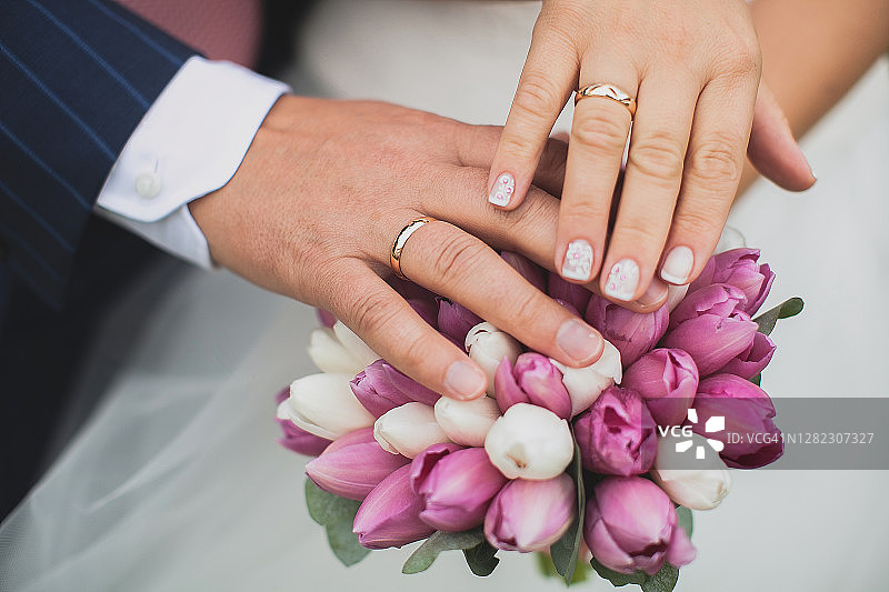 新郎和新娘的手捧着一个美丽的婚礼花束，上面有粉红色和白色的花，绿色的叶子。新婚夫妇在他们的婚礼上。图片素材