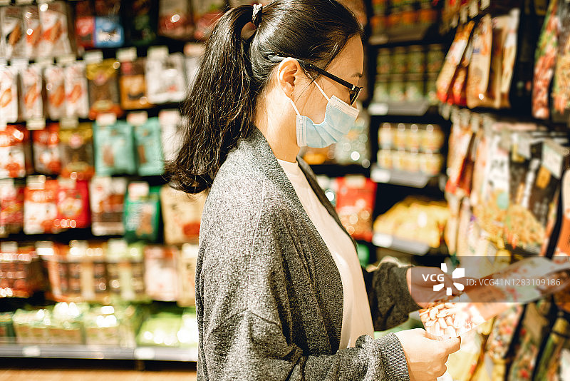 戴口罩的亚裔女人在超市挑选商品图片素材