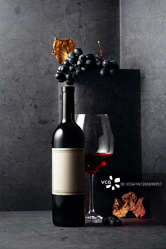 黑色的石头桌子上放着红酒和蓝色的葡萄，还有干枯的葡萄藤叶子。图片素材