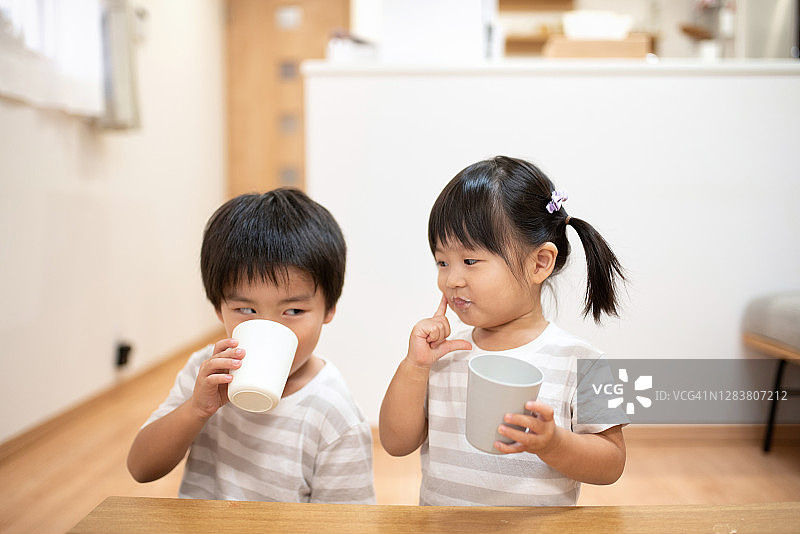 两个孩子，姐姐和哥哥一起在房间里喝着一杯牛奶图片素材