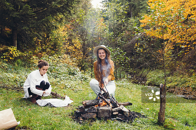 年轻的妇女们在森林里的篝火旁为明亮的野餐做准备图片素材
