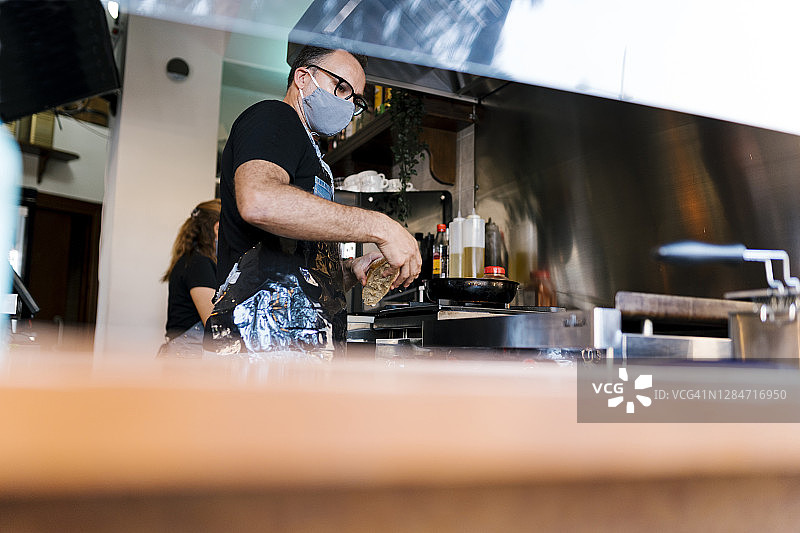 2019冠状病毒病期间，在咖啡吧厨房做饭时佩戴防护口罩的男咖啡师图片素材