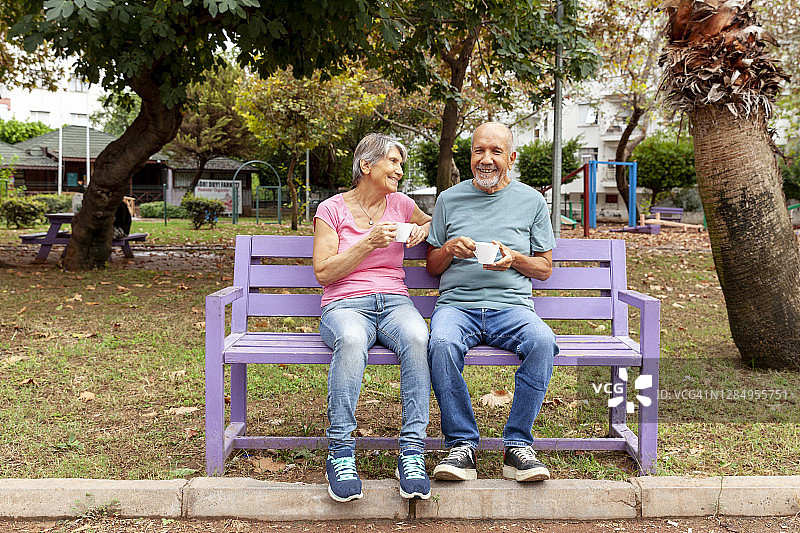 一对老夫妇坐在长凳上喝咖啡。图片素材