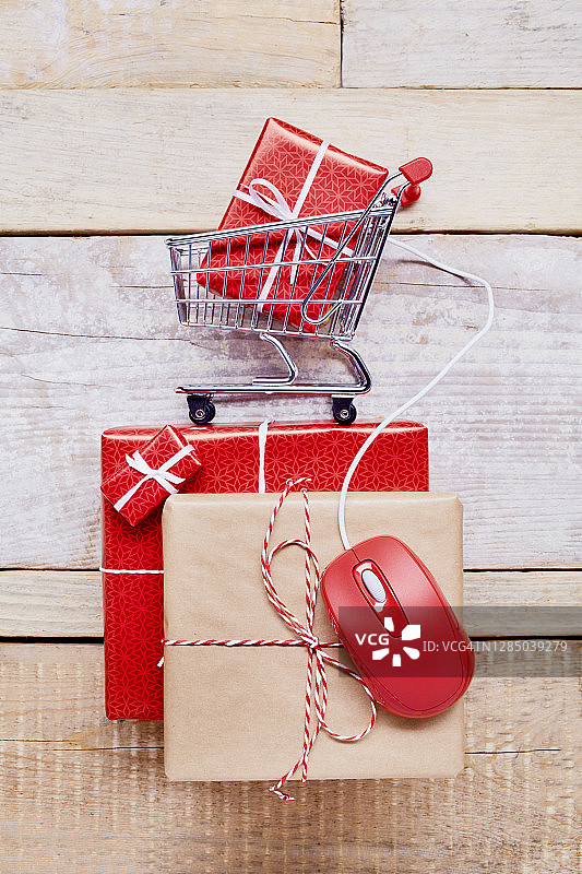 高角度的小购物车，圣诞礼物和红色电脑鼠标放在木桌上，网上购物图片素材
