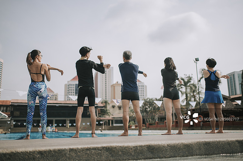后视图亚洲华人家庭做热身运动在游泳池上午与教练图片素材