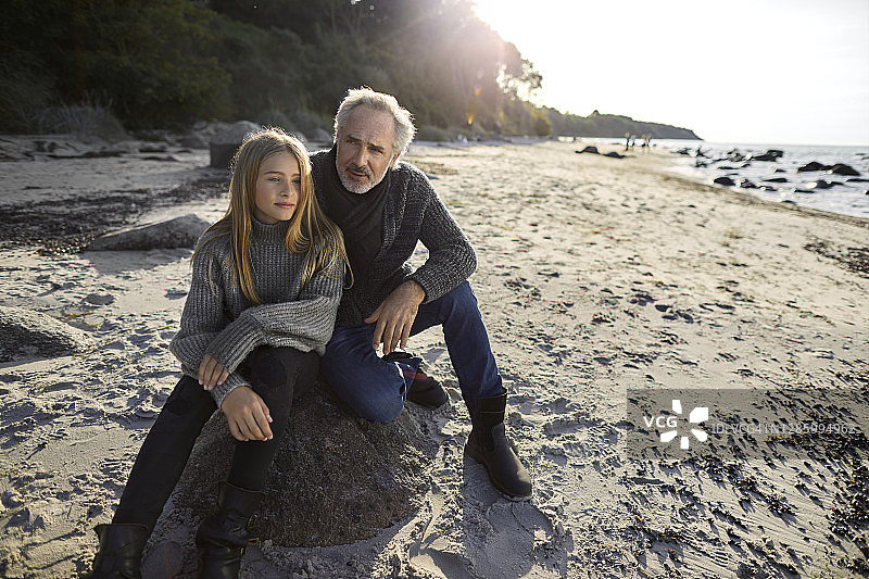 父亲和女儿坐在沙滩上的巨石上图片素材