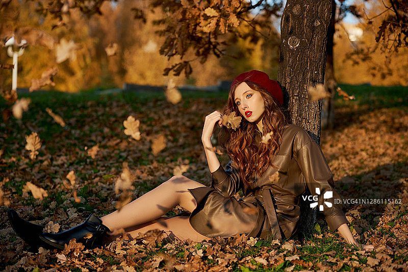一个女人在秋天的肖像帽子贝雷帽和雨衣附近的一棵树在秋天黄色的树叶图片素材