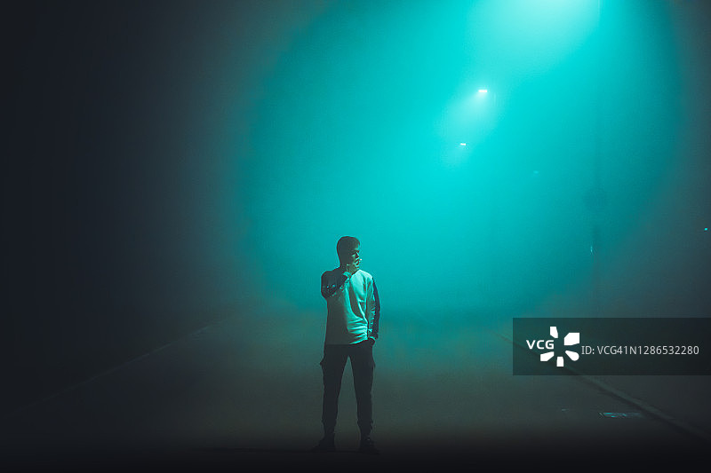 一个年轻人独自站在被灯光照亮的雾蒙蒙的街道上图片素材