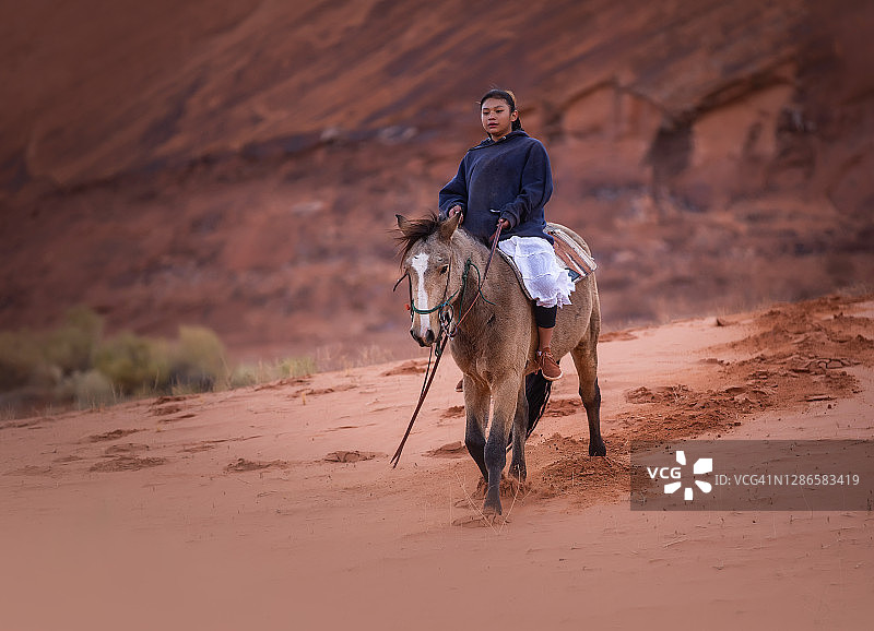 纳瓦霍土著女孩骑在沙丘上在亚利桑那沙漠纪念碑谷图片素材
