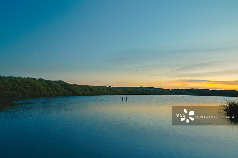 平静平静的湖日落与彩色天空的背景和平滑的倒影在水面上图片素材