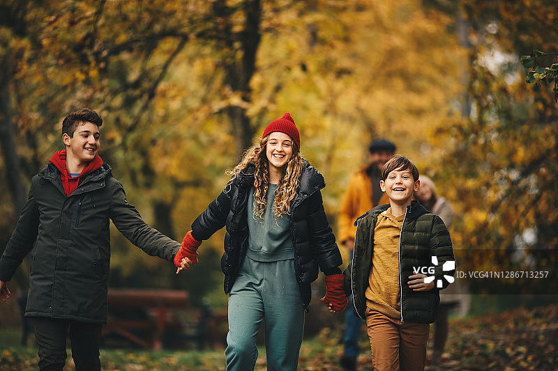 家人在秋天的森林里度过时光。孩子们手牵着手走在林中小路上。图片素材