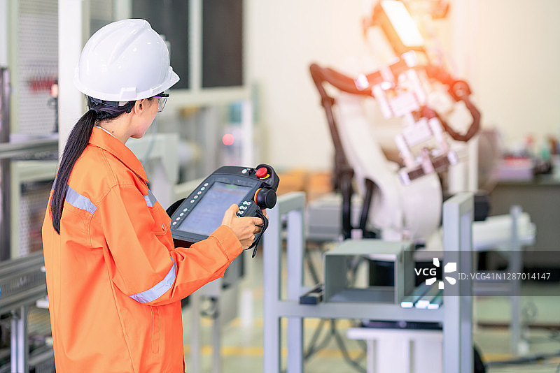 专业人员检查机器人在制造工厂的夹具基地上移动。在实验室修理机械臂，戴防护眼镜，使用控制器或机器人控制面板。图片素材