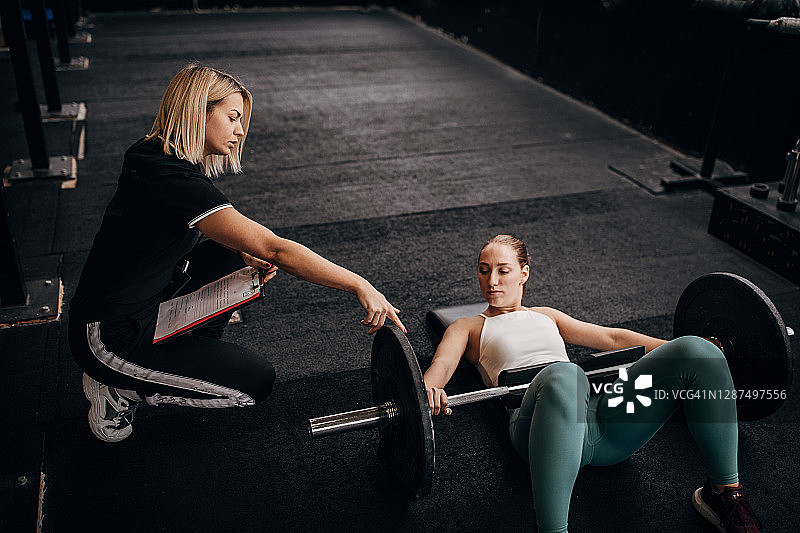 健身女性在她的私人教练的帮助下进行举重锻炼图片素材