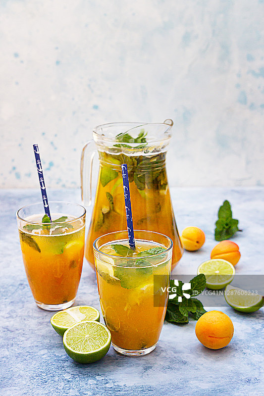 自制冰柠檬水或茶加杏，酸橙和薄荷。新鲜的杏味鸡尾酒在一个罐子和玻璃在蓝色混凝土背景。图片素材
