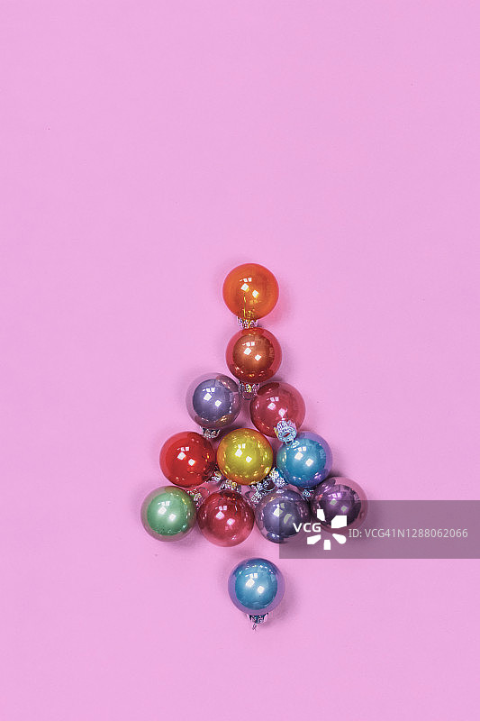 粉红色背景上的圣诞树形状的彩色圣诞装饰品。图片素材