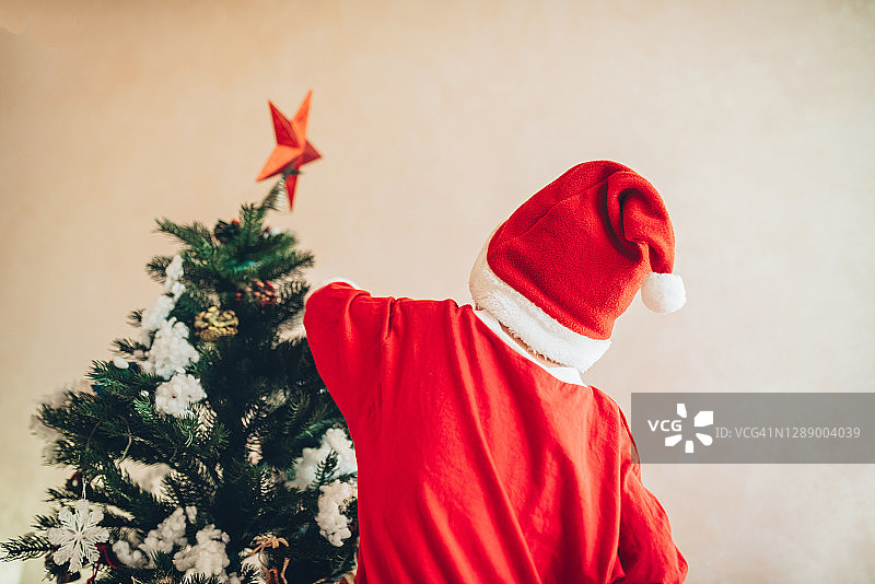 4-5岁男孩穿着圣诞服装在家装饰圣诞树。圣诞节庆祝活动的概念。图片素材