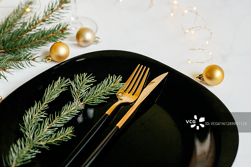 金色和黑色的刀叉在黑色的盘子和白色的背景。松树枝、蜡烛和装饰品。为圣诞节准备的节日餐桌。图片素材