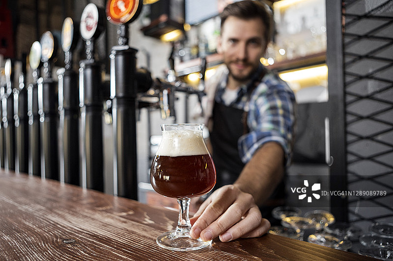 一个男人在酒吧里端啤酒，镜头对准啤酒杯图片素材