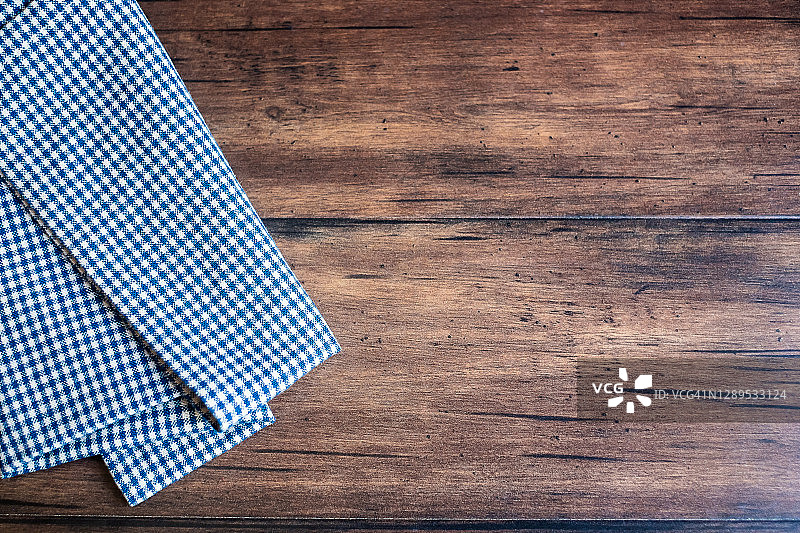 旧的棕色木制背景上的蓝色格子餐巾，俯视图。图像与复制空间。厨房桌子与毛巾顶视图与复印空间。图片素材