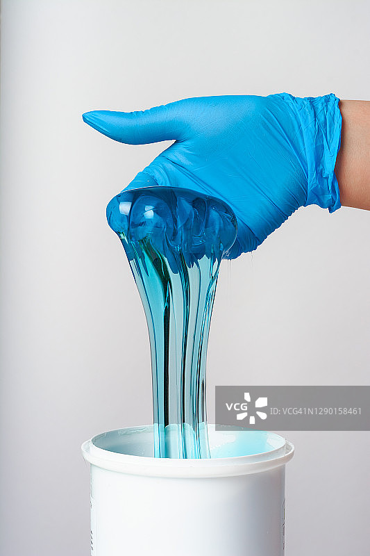 在美容院，一位戴着蓝色手套的大师手里拿着化妆品罐里的糖蜡。脱毛的概念。图片素材