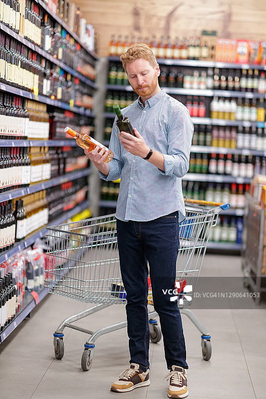 年轻人在超市里看标签来决定买哪种酒图片素材