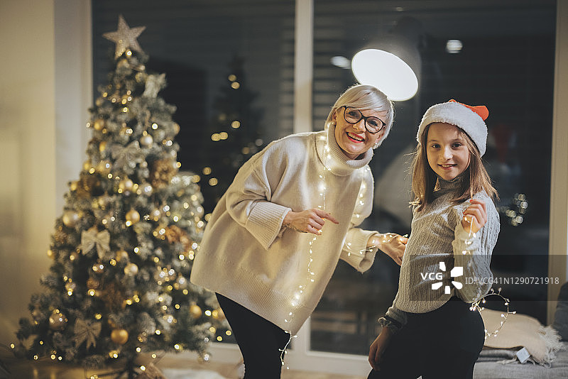 母亲和女儿微笑着，圣诞彩灯挂在他们的肩膀上图片素材