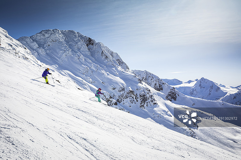 在阳光明媚的日子里，一对夫妇在精心设计的滑雪跑道上滑雪。图片素材