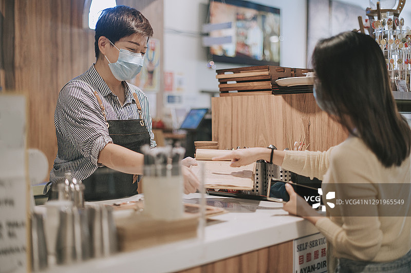 亚洲华人的咖啡馆老板，收银员，女商人面罩，从她的客户在柜台的订单图片素材