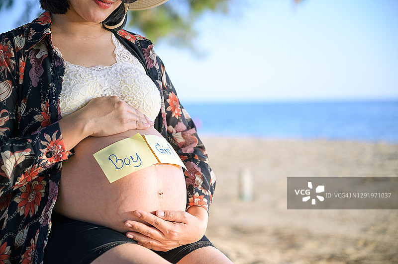 怀孕的亚洲妇女将“男孩”或“女孩”写在自己肚子上的纸上图片素材