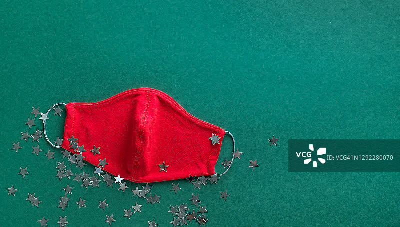 红色医用防护口罩和五彩纸屑在绿色圣诞背景上。预防和预防COVID - 19大流行的传播。预防病毒、感染和肺炎。一个快乐健康的圣诞理念。图片素材