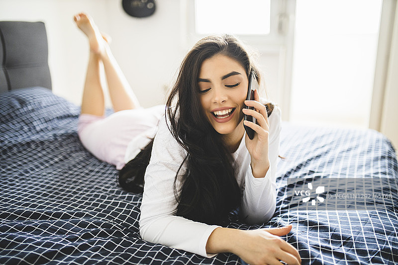 微笑的女人躺在床上休息时使用智能手机图片素材