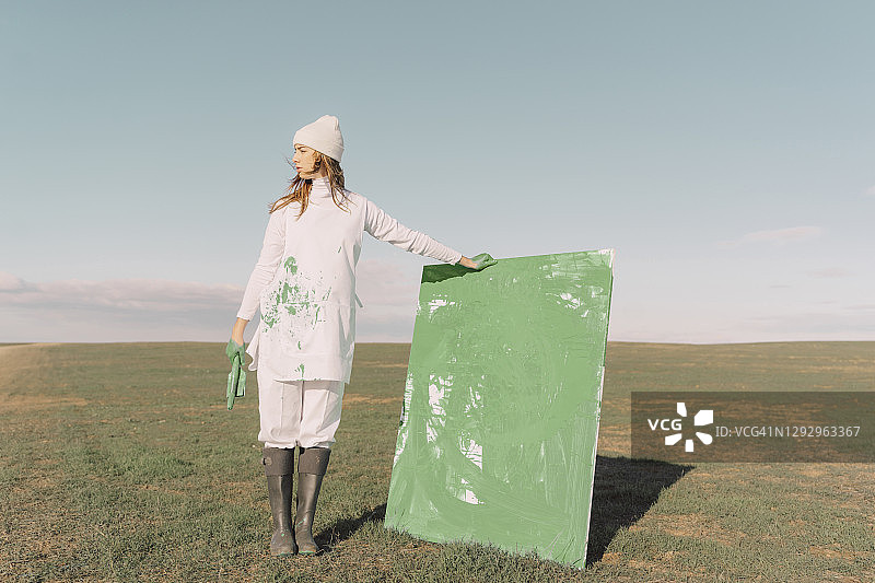 年轻女子在干燥的土地上拿着绿色的画图片素材