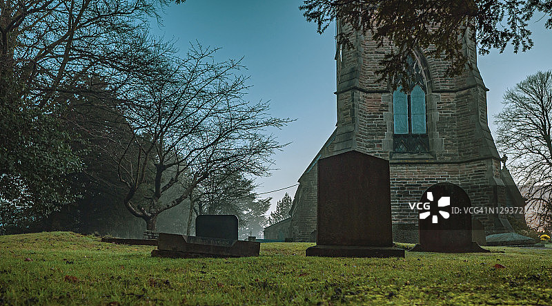 广角拍摄一个朦胧的教堂和墓碑。图片素材